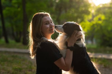 Beyaz bir kadın parkta yürürken köpeğine sarılıyor.