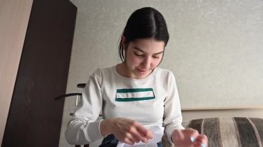 Genç beyaz kadın yatakta otururken çapraz dikiş atıyor.