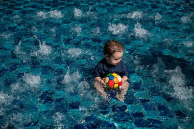 Bir yaşında beyaz çocuk yüzme havuzunda top oynuyor.