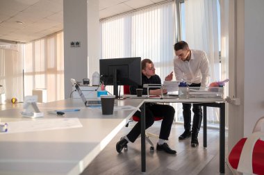 Beyaz adam çalışma masasında durmuş iş hakkında konuşuyor.