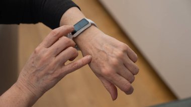 Kafkasyalı yaşlı bir kadın akıllı saate bakıyor. Ellerin yakın çekimi