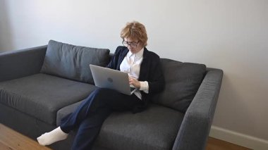 Yaşlı, ciddi bir iş kadını dizüstü bilgisayarla koltukta oturuyor.