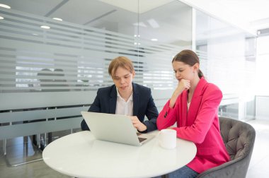 Meslektaşlar aynı masada oturup dizüstü bilgisayara bakıyorlar.
