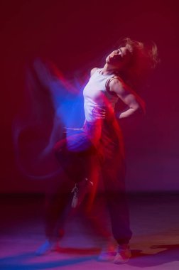 Genç bir kadın mavi ve kırmızı ışıkta çağdaş dans ediyor. Uzun pozlama. Dikey fotoğraf