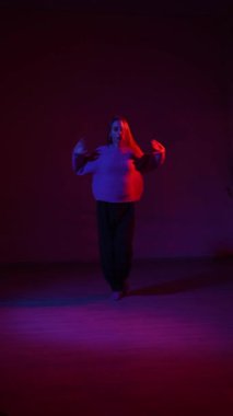 A young woman dances contemporary dances in blue and red light. Long exposure. Vertical video