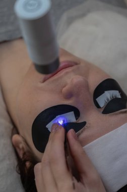 Kirpik uzatma prosedüründen geçen bir kadın ultraviyole lamba kullanıyor.