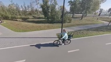 Beyaz bir kadın parkta küçük oğluyla bisiklete biniyor.