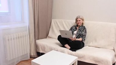 Kanepede otururken laptop kullanan olgun bir kadın.