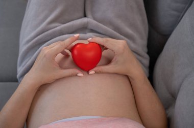 Beyaz, hamile, karnı üzerinde kalbi olan bir kadın. Üçüncü üç aylık dönem