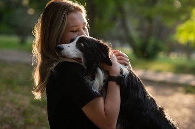 Beyaz bir kadın parkta yürürken köpeğine sarılıyor.