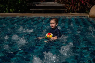 Bir yaşında beyaz çocuk yüzme havuzunda top oynuyor.