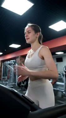 Beyaz kadın spor salonunda koşu bandında koşuyor.