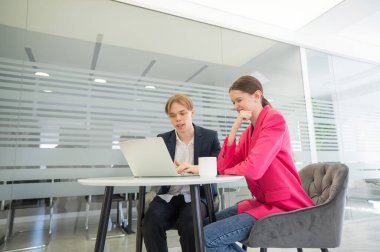 Meslektaşlar aynı masada oturup dizüstü bilgisayara bakıyorlar.