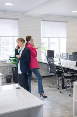 İki meslektaş sırt sırta durup telefonlarıyla konuşur.