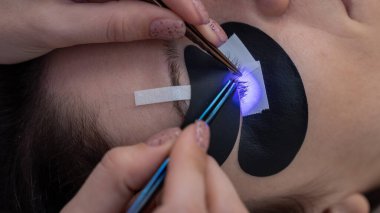 Kirpik uzatma prosedüründen geçen bir kadın ultraviyole lamba kullanıyor.