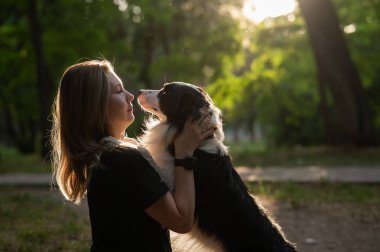 Beyaz bir kadın parkta yürürken köpeğine sarılıyor.