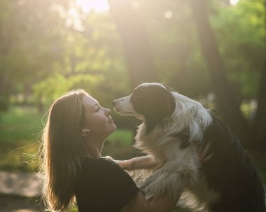 Beyaz bir kadın parkta yürürken köpeğine sarılıyor.