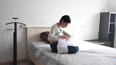 Genç beyaz kadın yatakta otururken çapraz dikiş atıyor.