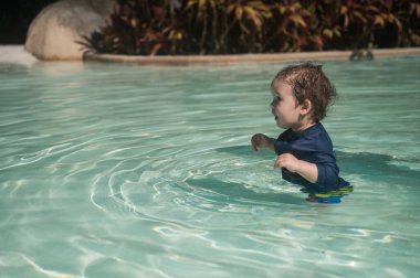 Bir yaşında beyaz bir çocuk kumlu poposu olan bir havuzda yüzüyor.