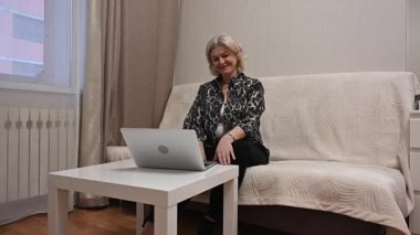 Kanepede otururken laptop kullanan olgun bir kadın.