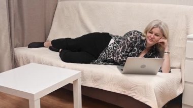 Kanepede yatarken laptop kullanan olgun bir kadın.