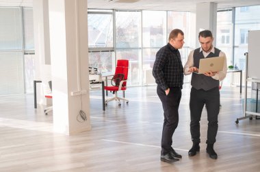 İki beyaz adam dizüstü bilgisayara bakıyor ve iş tartışıyorlar.