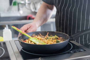 Şef tavada makarna pişirir.