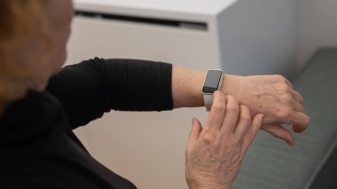 Kafkasyalı yaşlı bir kadın akıllı saate bakıyor. Ellerin yakın çekimi
