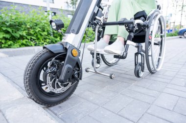 Tekerlekli sandalyedeki yüzü olmayan ve manuel kontrol için yardımcı bir aleti olan bir kadın. Elektrikli bisiklet.