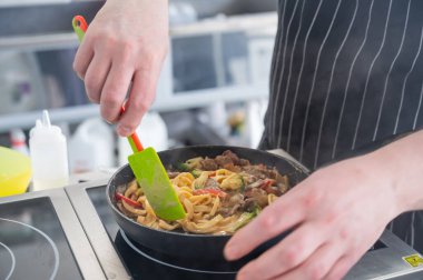 Şef tavada makarna pişirir.