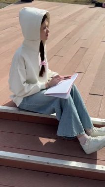 Açık havada kalemle çizim yapan beyaz bir kadın.