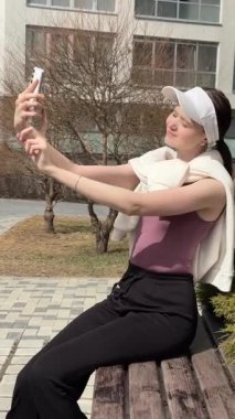 Genç beyaz kadın yürürken selfie çekiyor.