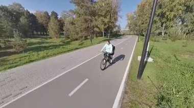 Beyaz bir kadın parkta küçük oğluyla bisiklete biniyor.