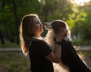 Beyaz bir kadın parkta yürürken köpeğine sarılıyor.