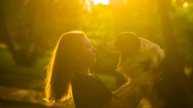 Beyaz bir kadın parkta yürürken köpeğine sarılıyor.