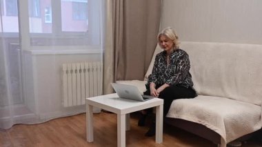 Kanepede otururken laptop kullanan olgun bir kadın.