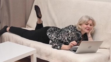 Kanepede yatarken laptop kullanan olgun bir kadın.