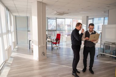 İki beyaz adam dizüstü bilgisayara bakıyor ve iş tartışıyorlar.