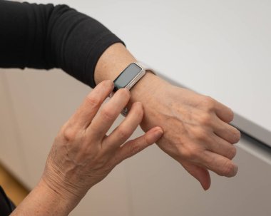 Kafkasyalı yaşlı bir kadın akıllı saate bakıyor. Ellerin yakın çekimi