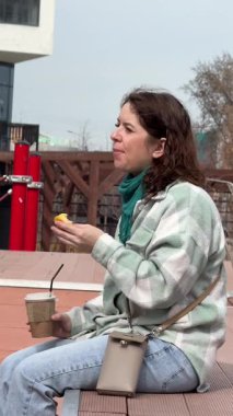 Beyaz kadın kruvasan yiyor ve dışarıda kahve içiyor.