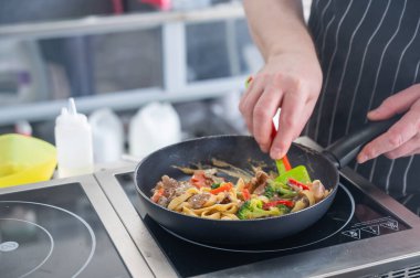 Şef tavada makarna pişirir.