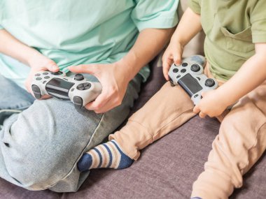 Beyaz kadın küçük oğluna konsol oynamayı öğretiyor. Oyun kolu ellerinde.