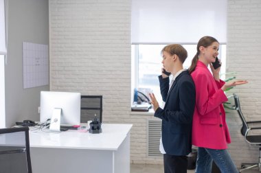 İki meslektaş sırt sırta durup telefonlarıyla konuşur.