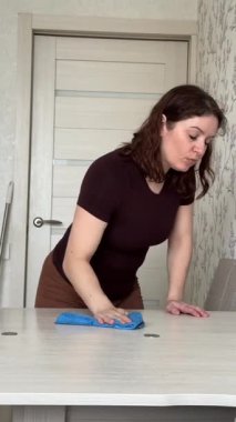 Beyaz kadın yemek masasını bezle siliyor.