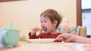 Şirin bir çocuk tek başına yulaf lapası yiyor.