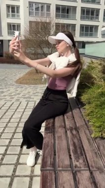 Genç beyaz kadın yürürken selfie çekiyor.