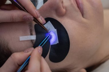 Kirpik uzatma prosedüründen geçen bir kadın ultraviyole lamba kullanıyor.