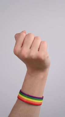 Gökkuşağı bileziği takan kadın parmaklarıyla kalp hareketi yapıyor.