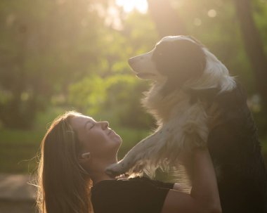 Beyaz bir kadın parkta yürürken köpeğine sarılıyor.