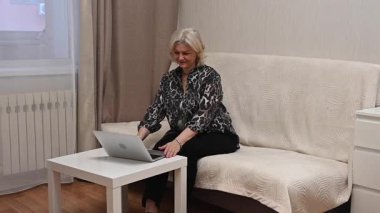 Kanepede otururken laptop kullanan olgun bir kadın.